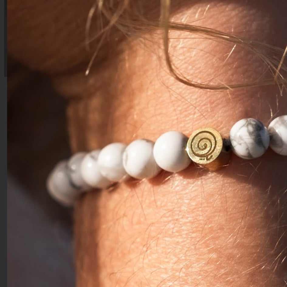 White howlite NEMDAE bracelet and its gold Gratitude Symbol worn on a wrist